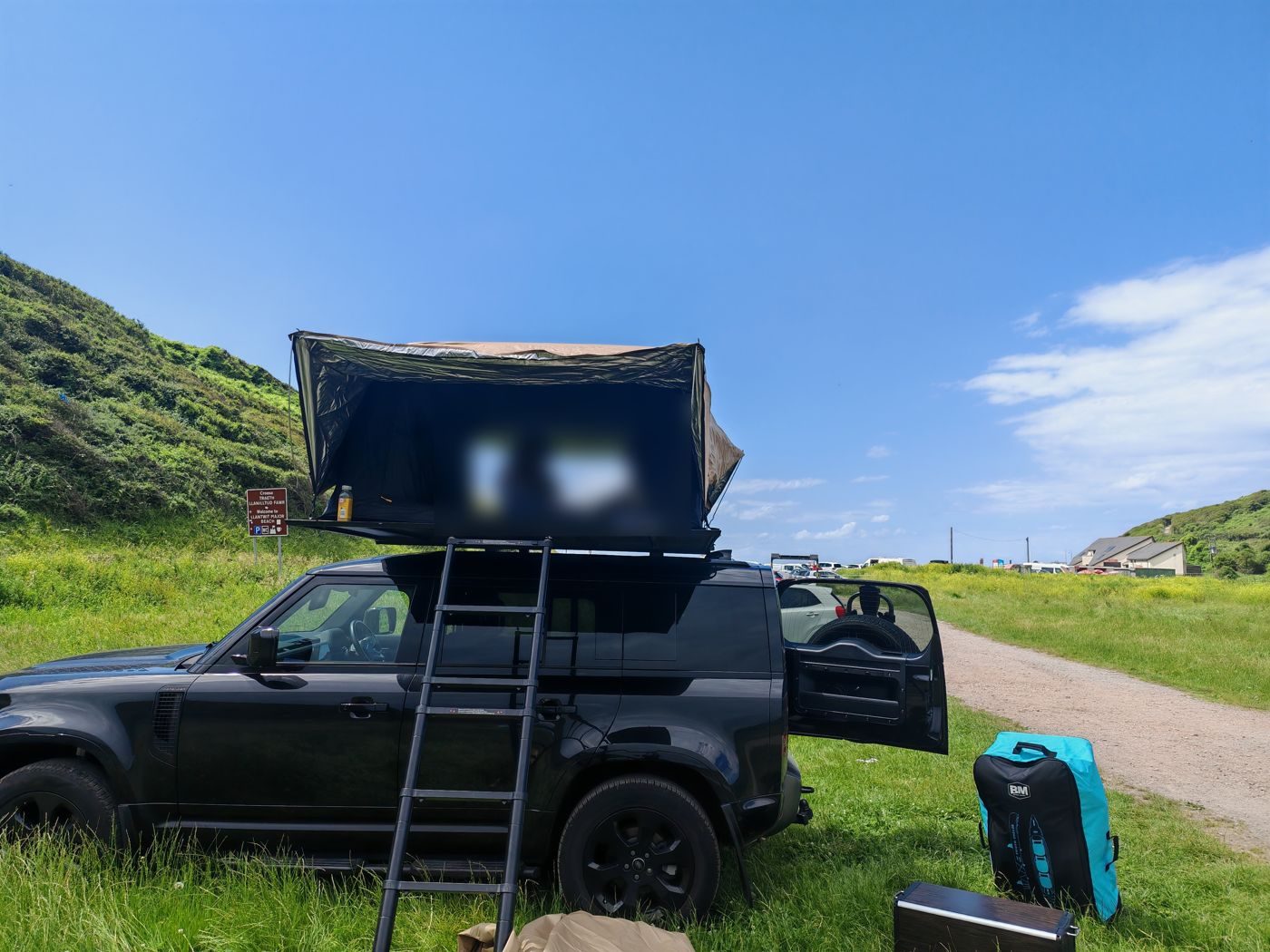 Open aluminium roof tent on a Land Rover Defender above a Welsh beach car park